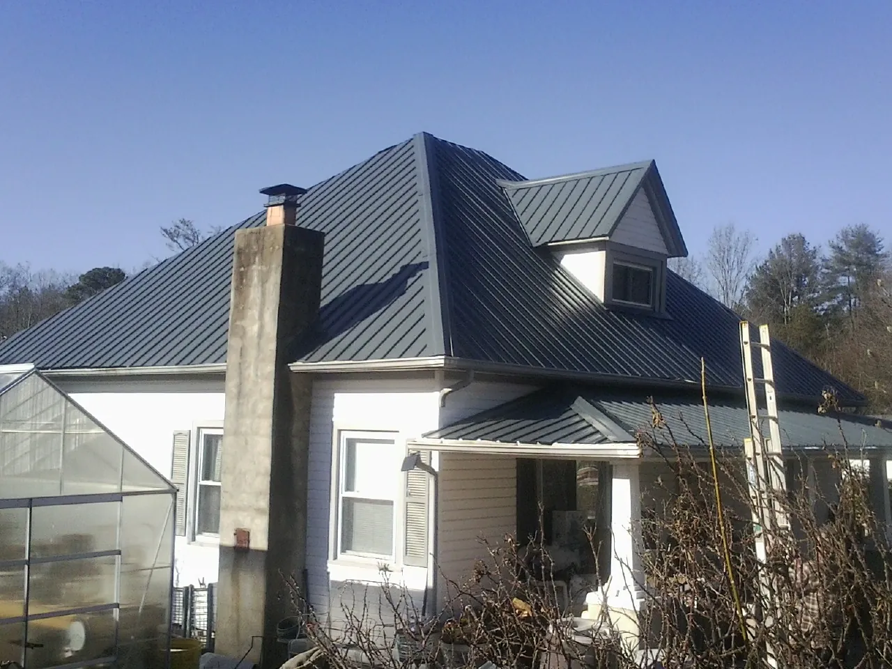 Dark blue standing seam metal roof on a white farmhouse with dormer — Slate & Tile Roof Repair by Roofing Brothers in New Hill