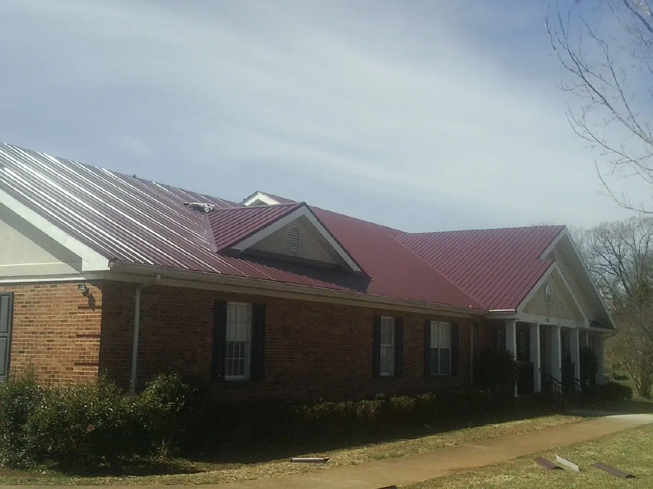 Red metal roof with gabled entries on a long brick building, from a Hail Damage Roof Repair job in New Hill