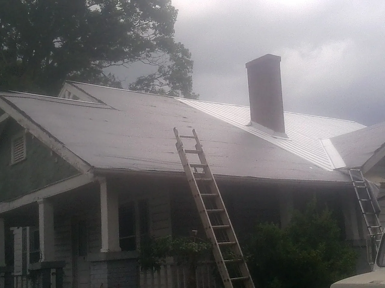 Ladders against a metal roof on an older home with a brick chimney in New Hill