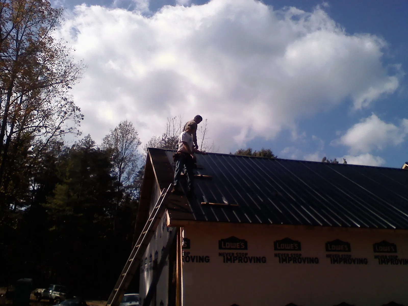 Roofer fastening dark metal panels high against a cloudy sky, from a Roof Inspection job in New Hill