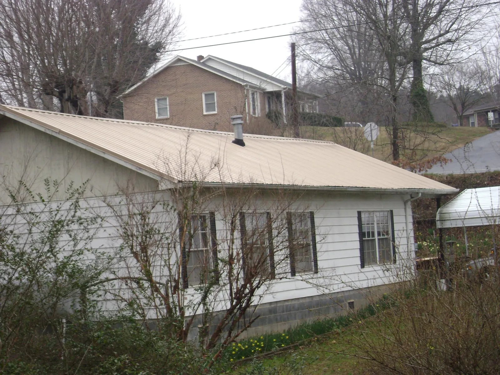 Tan metal roof on a white sided house set into a hillside — Commercial Roofing by Roofing Brothers in New Hill
