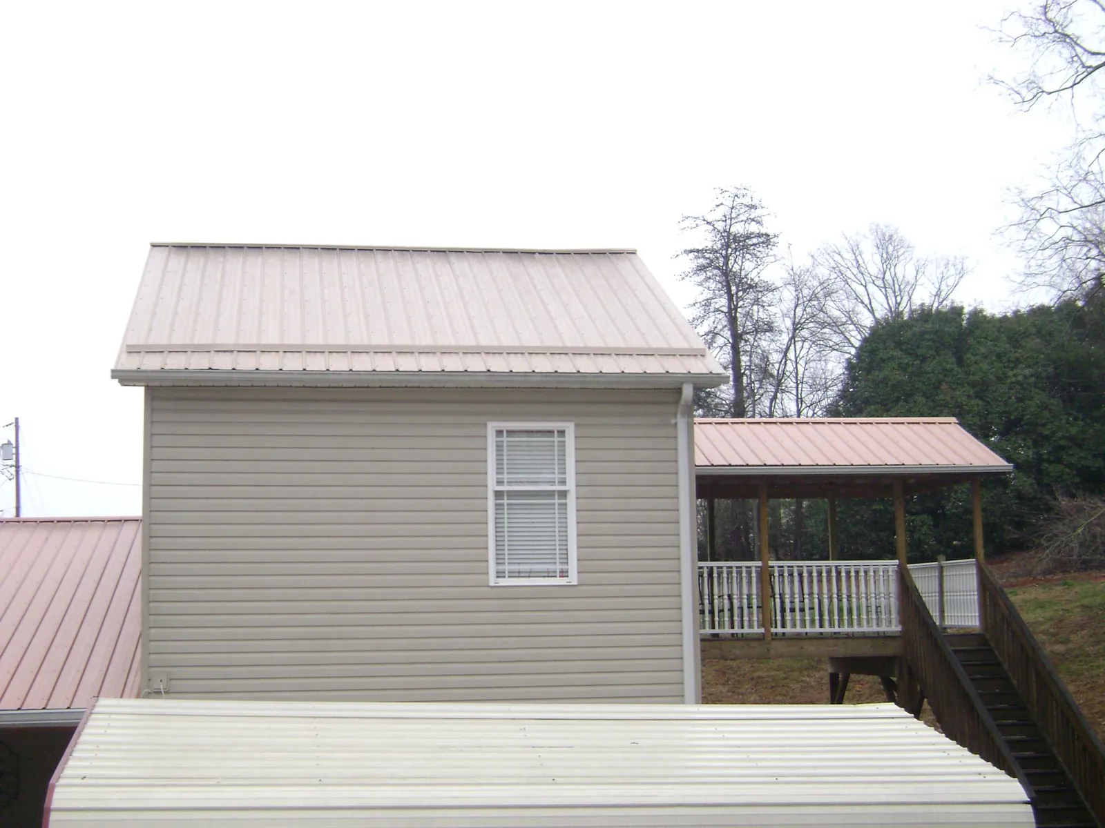 Tan metal roofs on a two story addition and attached porch, from a Roof Replacement job in New Hill